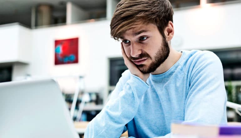 A man in a blue shirt looks at a computer with skepticism or even disgust