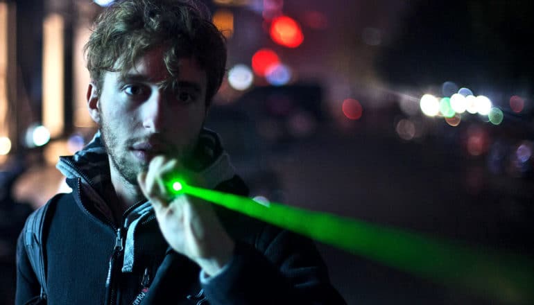 A man shines a green laser pointer on the street at night