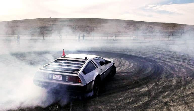 MARTY, the self-driving DeLorean, drifts on a open course, kicking up lots of smoke and making black tire marks on the pavement