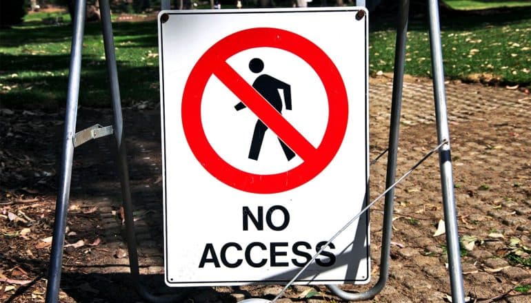 A sign with a red cross over an image of a person above the words "No Access" sits on a park path