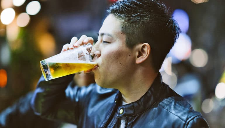east asian man drinks glass of beer
