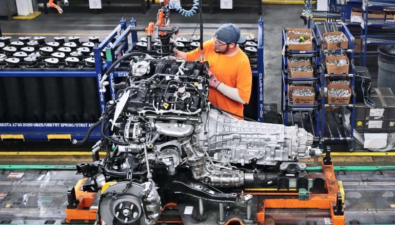 auto worker with car engine on plant floor