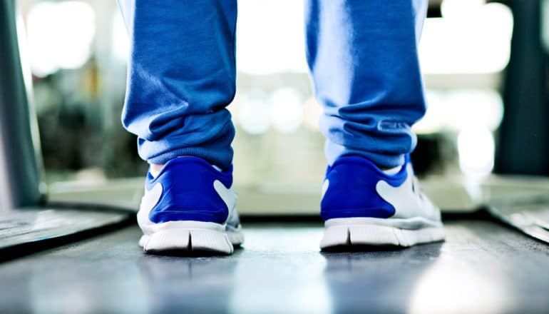 A person stands on a treadmill in blue shoes and blue sweatpants