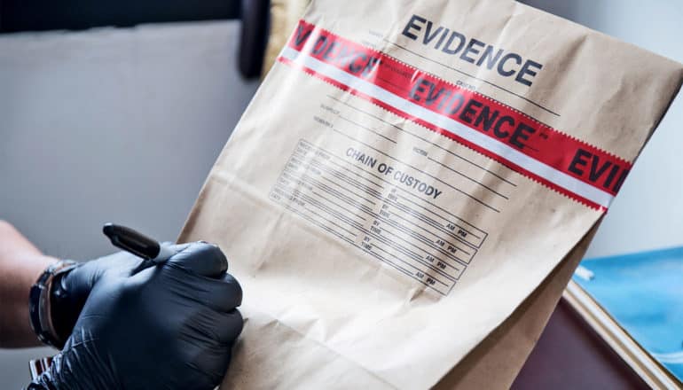 A person in black gloves writes on a brown paper evidence bag