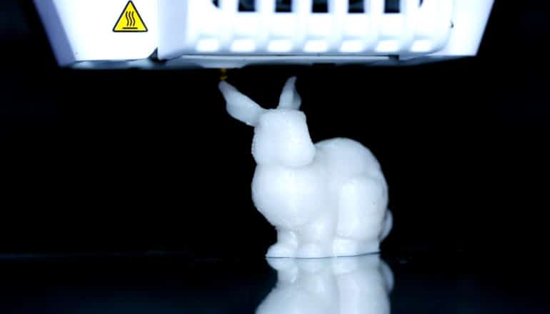 A white, 3D-printed rabbit sits on reflective surface with a black background