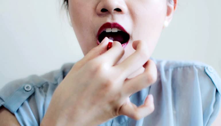 A woman is about to swallow a red pill as she holds it up to her mouth