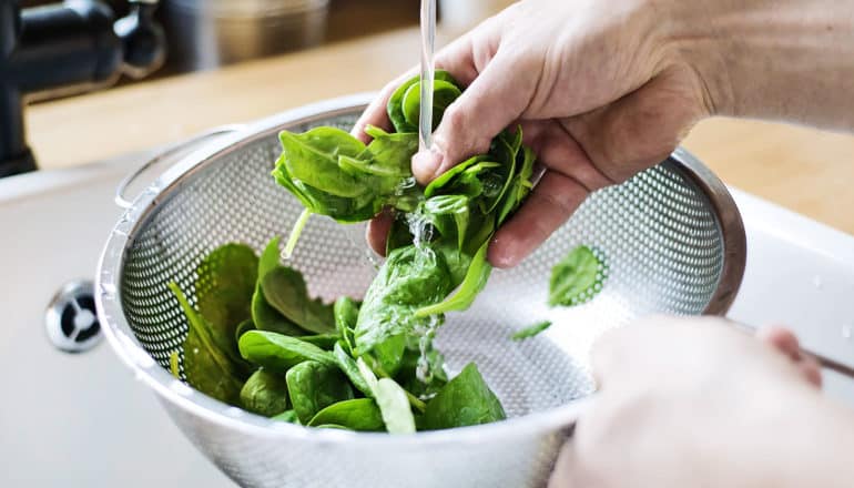 A person washes spinach in a colander.