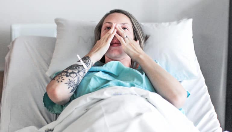 pregnant woman wipes tears from eyes in hospital bed