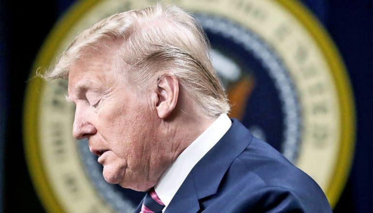 President Trump looks down, shot in profile in front of the presidential seal