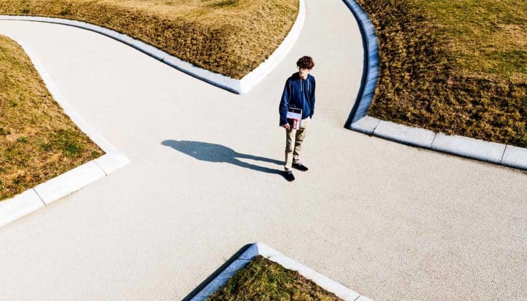 A young man stands at a four-way crossroad, looking around to pick a direction