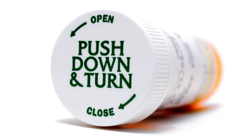 A pill bottle sits on its side with its lid on, reading "Push down & turn"