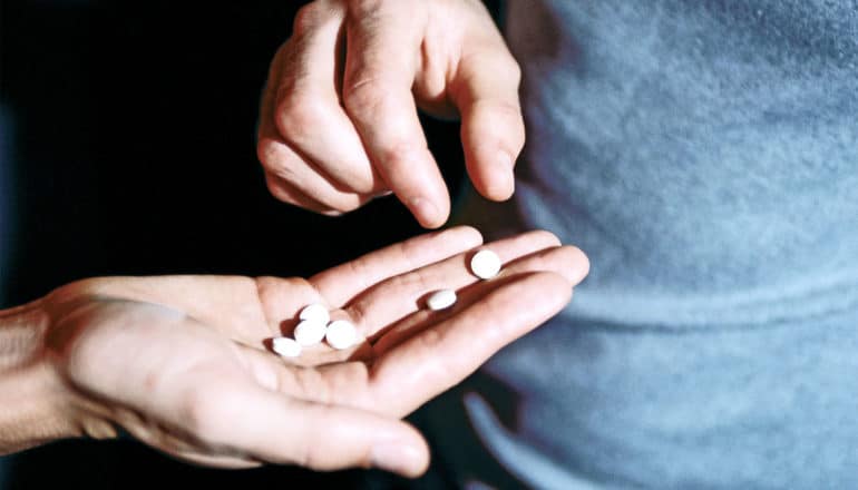 One person's hand holds a bunch of white pills while another person grabs for one