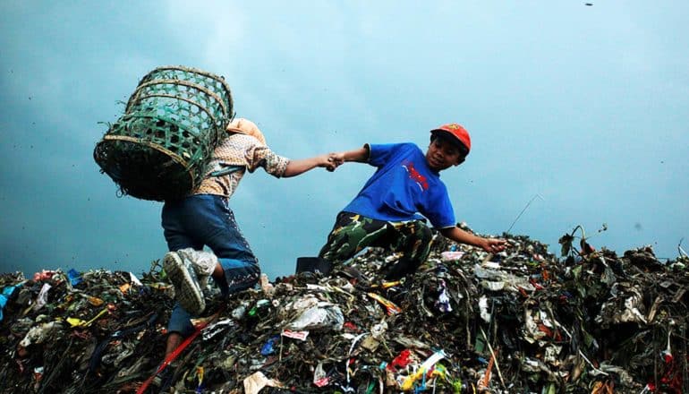two children atop mountain of trash, one wearing basket on back