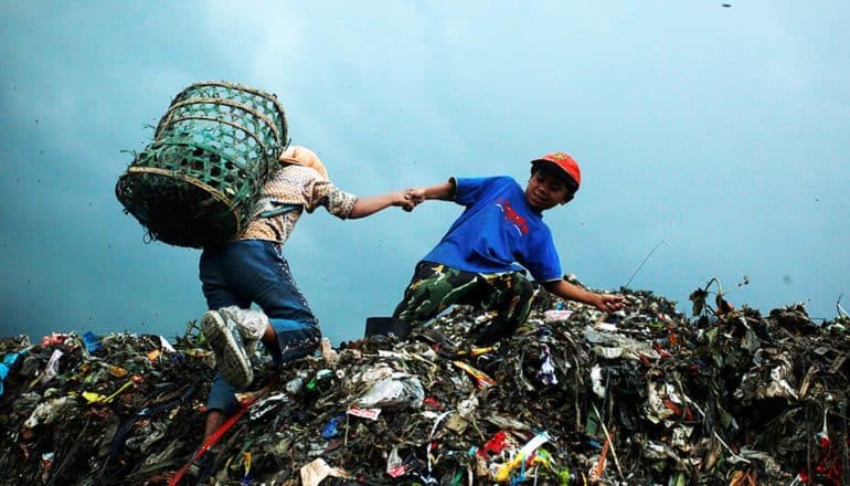 two children atop mountain of trash, one wearing basket on back
