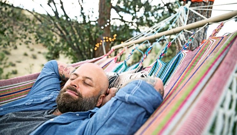 A man in blue lays on a hammock with his hands behind his head