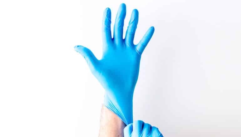 A person pulls on a blue medical glove showing five fingers