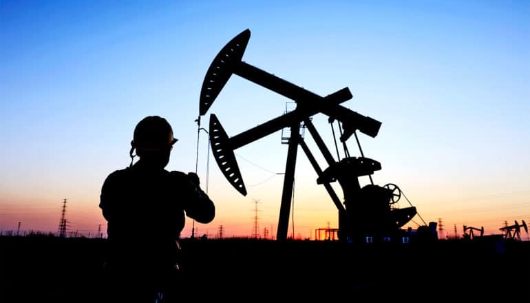 An oil worker stands in silhouette near a rig at sunset
