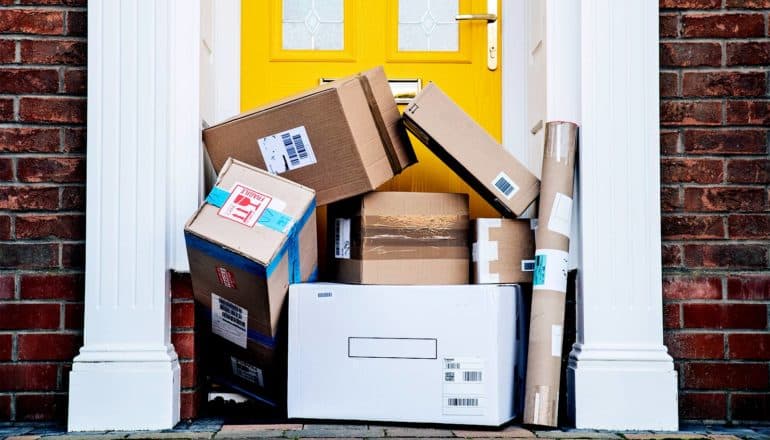 A large number of big packages on a doorstep partially covers the yellow door, filling the white door frame.