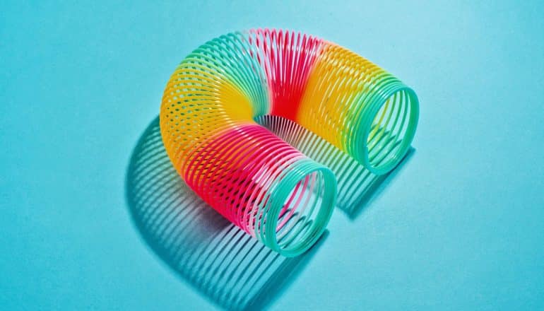 A rainbow-colored slinky is bent into a rainbow shape on a blue background