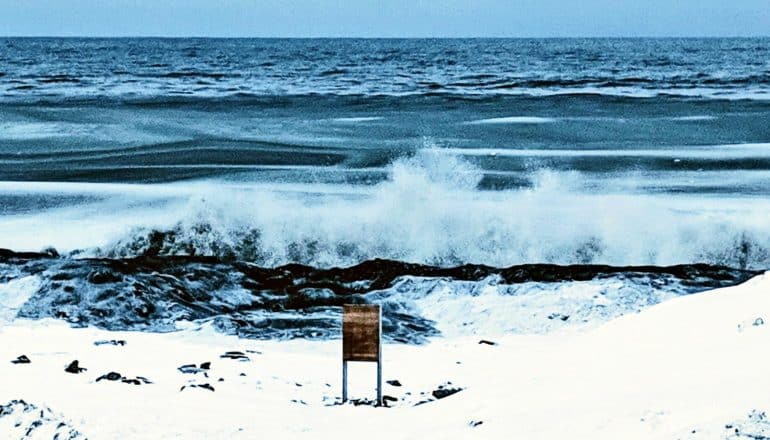 A wave breaks on a white and snowy Arctic shore