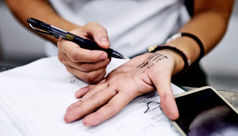 A person writes themselves a note on their hand in pen