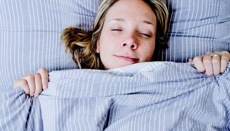 A woman looks like she's waking up rested under a blue striped comforter with her eyes just starting to open