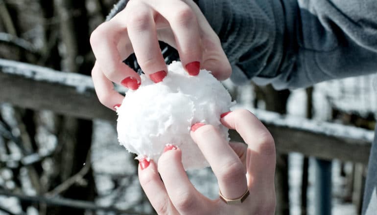 hands hold snowball with red-painted fingernails