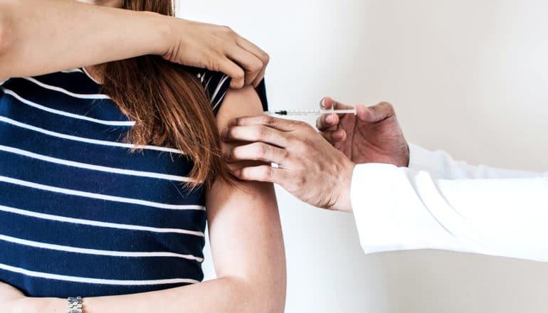 A woman in a navy shirt with white stripes gets a vaccine from a doctor in a white coat.