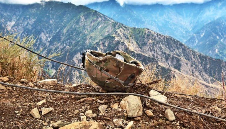 A combat helmet sits on a mountain side in Afghanistan, with more mountains in the background
