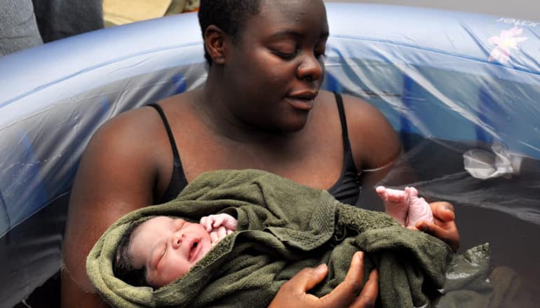 woman in birthing pool holds newborn in towel