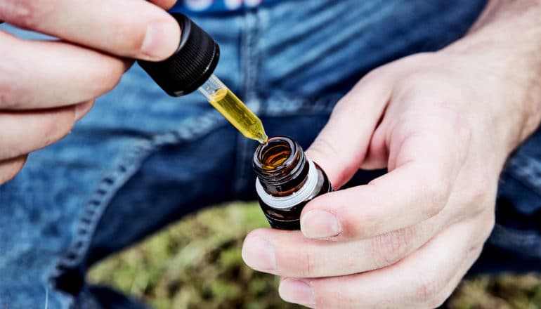 A person removes a full dropper from a small bottle of CBD oil