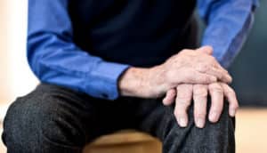 older person holds hand down on knee, as if to quell tremor