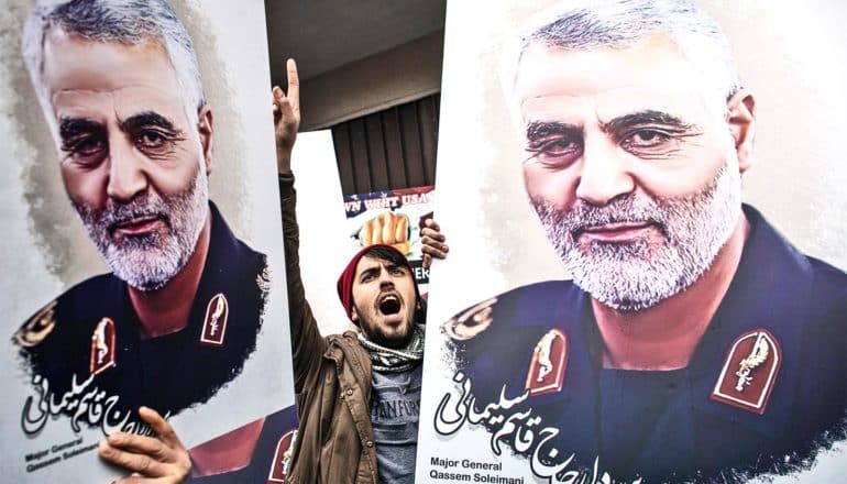 Protestors hold up Soleimani's portrait on large posterboards, with one young man raising his hand and shouting