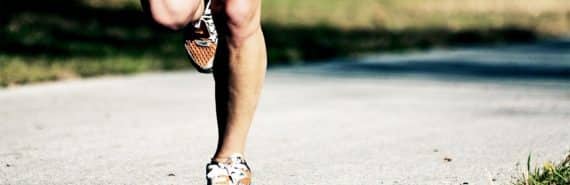 A person runs down a park path with grass on either side wearing orange running shoes, only their legs visible in the frame.