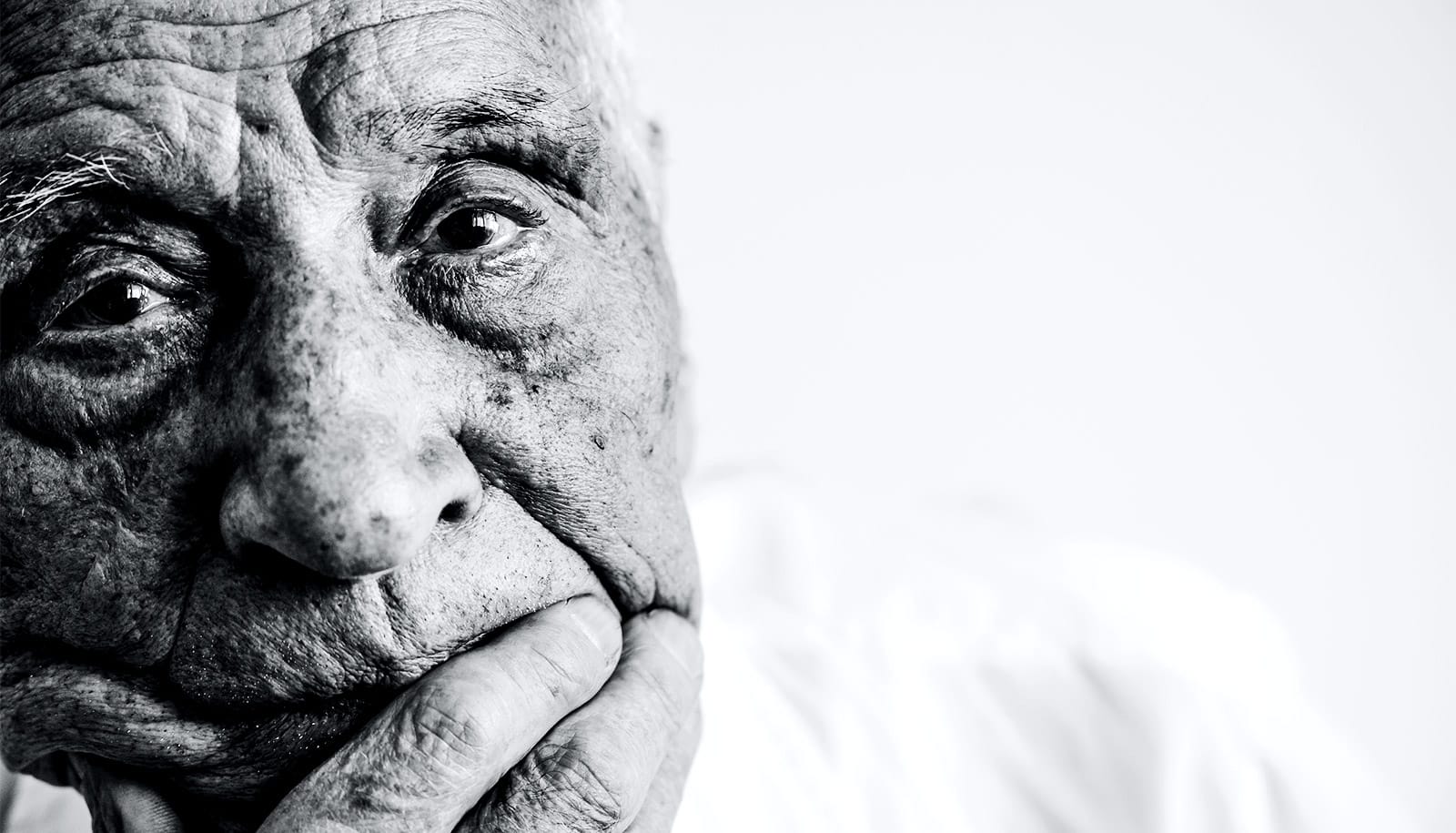 An older man looks sad as he puts his hand to his chin
