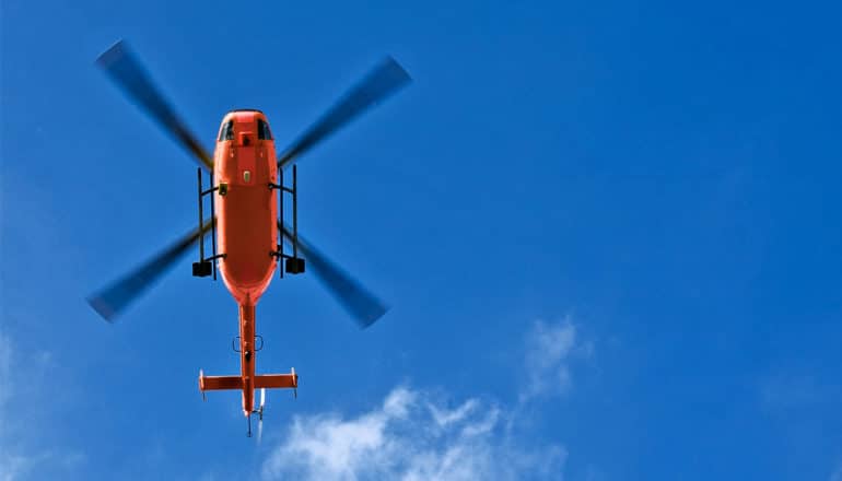 An red air ambulance helicopter flies in a deep blue sky, seen from below