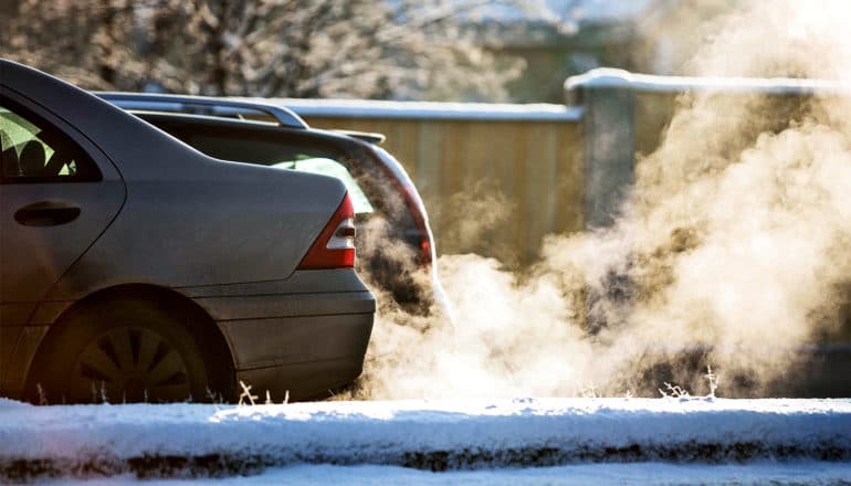 Cars spew exhaust while driving on a wintery road