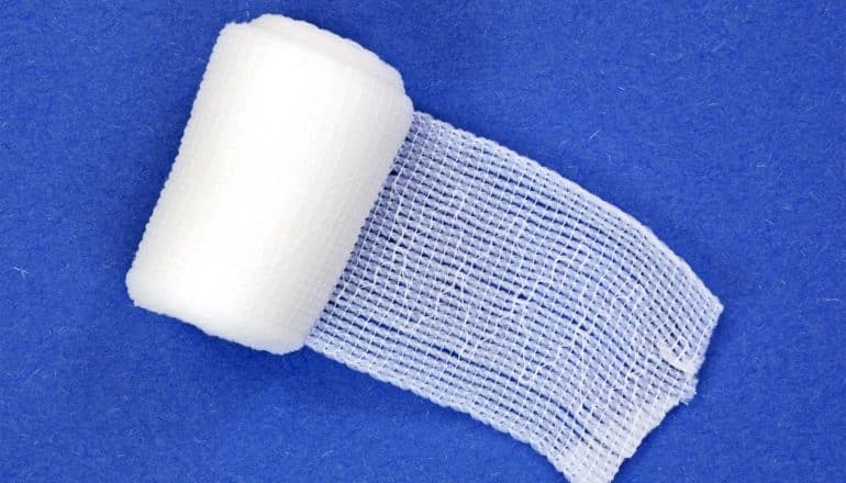 A roll of gauze bandage unfurls on a blue background