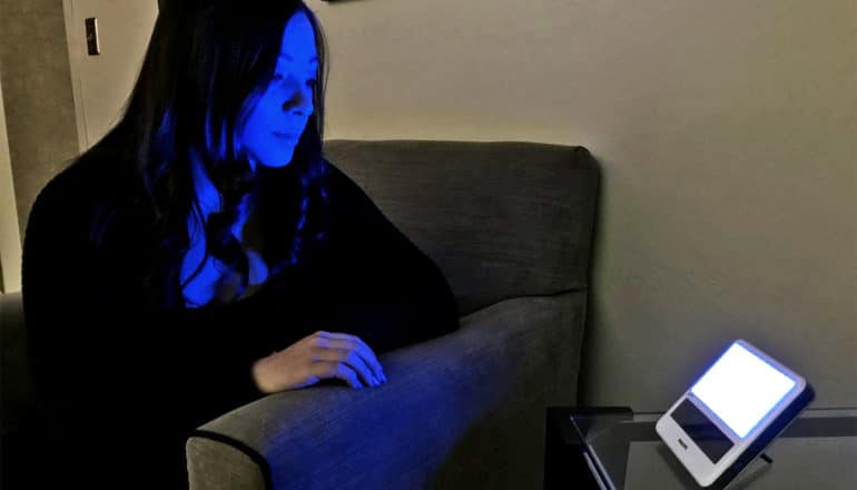 A researcher is illuminated in blue light by a small device on a sidetable next to her chair