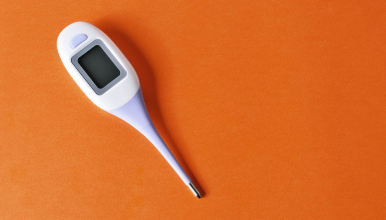 A digital thermometer sits on an orange background