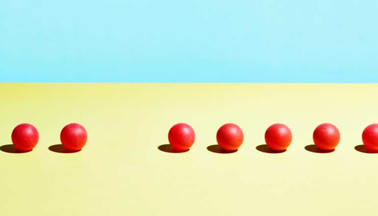 A row of red balls sits on a yellow surface with a blue background, with one ball missing from the series