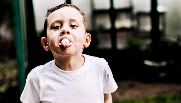 A young boy in a white t-shirt sticks his tongue out to the camera