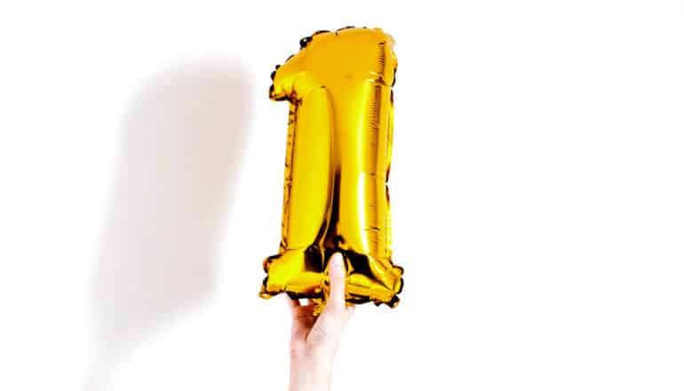 A hand holds up a yellow balloon in the shape of a number one