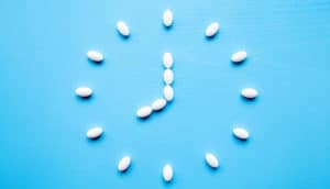White pills form the shape of a clock pointing to 9 o'clock on a blue background