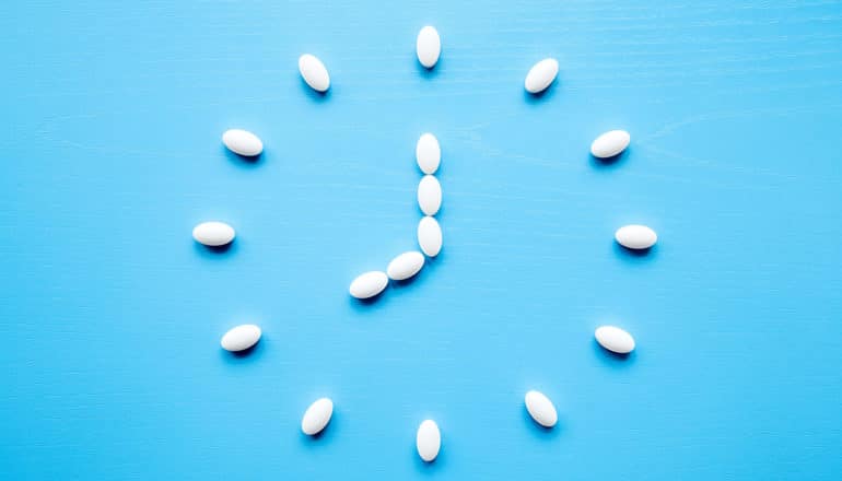 White pills form the shape of a clock pointing to 9 o'clock on a blue background