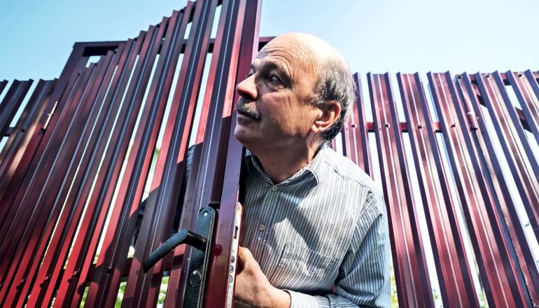 A man opens a fence door and looks out to his right