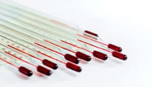 A set of 10 glass thermometers sit together at a diagonal angle on a white background