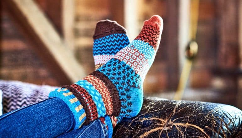 A person wearing colorful socks puts their feet up on the arm of a couch