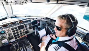 A pilot in the cockpit of an airplane wears sunglasses and a headset