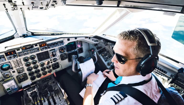 A pilot in the cockpit of an airplane wears sunglasses and a headset